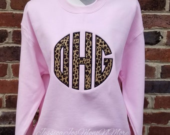May include: Pink sweatshirt with a large, black, circular monogram with a leopard print design. The monogram is the letters "D H G".