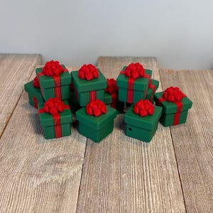 May include: A collection of small, green gift boxes with red ribbon and bows. The boxes are square-shaped and arranged on a wooden surface. The red bows are prominently displayed on top of each box, creating a festive appearance.