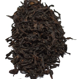 May include: A pile of dark brown loose leaf tea against a white background. The tea leaves have a twisted, dried appearance, suggesting a robust flavor profile. The image highlights the texture and color of the tea, perfect for tea enthusiasts.