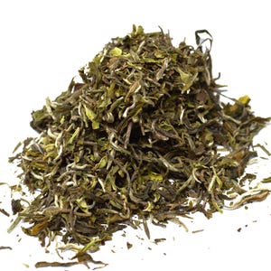 May include: A mound of loose-leaf white tea consisting of dried, curled, and twisted tea leaves in shades of olive green, brown, and pale silver-white. The texture is fibrous and delicate, with visible small buds and fragmented leaf pieces.