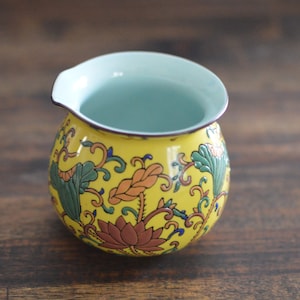 Könnte beinhalten: Eine gelbe Teekanne aus Keramik mit hellblauem Innenraum und einem floralen Design in Grün-, Orange- und Blautönen.