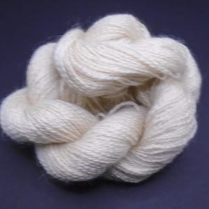 May include: A skein of off-white yarn, made of natural fibers, is twisted into a knot. The yarn is soft and fluffy, and it is perfect for knitting or crocheting.