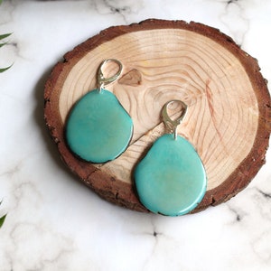 May include: A pair of turquoise blue earrings with silver hooks. The earrings are shaped like a teardrop and have a smooth, glossy finish.