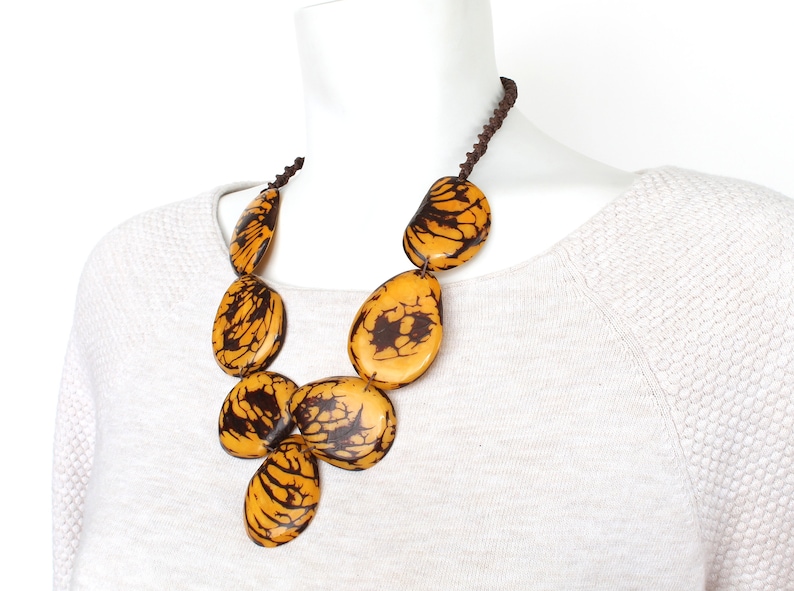 May include: A necklace made of large, oval-shaped, yellow and brown patterned beads. The beads are strung on a brown cord.