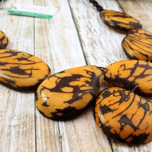 May include: A necklace made of large, oval-shaped, brown and yellow patterned beads. The beads are strung on a black cord.