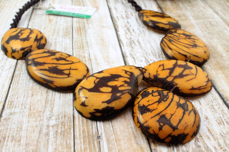 May include: A necklace made of large, oval-shaped, brown and yellow patterned beads. The beads are strung on a black cord.