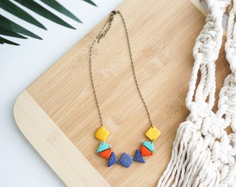 Op de afbeelding: Een kleurrijke houten ketting met geometrische vormen in tinten geel, blauw, oranje en groen. De ketting is gemaakt van hout en heeft een metalen ketting.