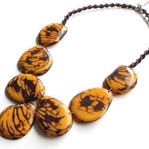 May include: A necklace made of brown cord with large, yellow and brown patterned beads. The beads are irregularly shaped and have a natural, organic look.
