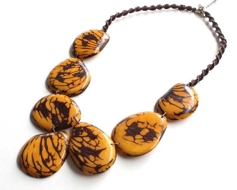 May include: A necklace made of brown cord with large, yellow and brown patterned beads. The beads are irregularly shaped and have a natural, organic look.