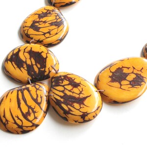 May include: A necklace made of large, yellow and brown, irregularly shaped beads. The beads have a marbled pattern.