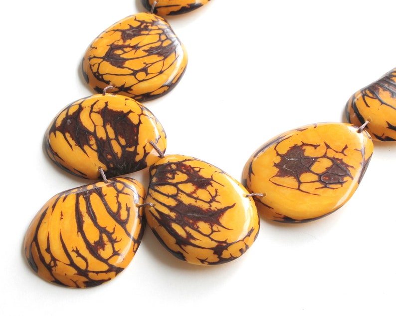 May include: A necklace made of large, yellow and brown, irregularly shaped beads. The beads have a marbled pattern.