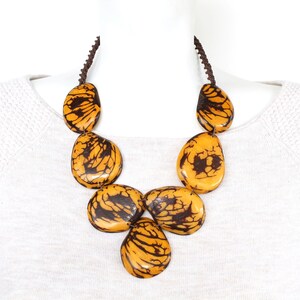 May include: A necklace made of large, teardrop-shaped beads. The beads are a light brown color with dark brown marbling. The necklace is strung on a brown cord.