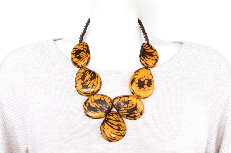 May include: A necklace made of large, teardrop-shaped beads. The beads are a light brown color with dark brown marbling. The necklace is strung on a brown cord.
