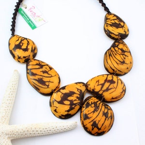 May include: A necklace made of large, teardrop-shaped, yellow and brown seed pods. The necklace is strung on a black cord.