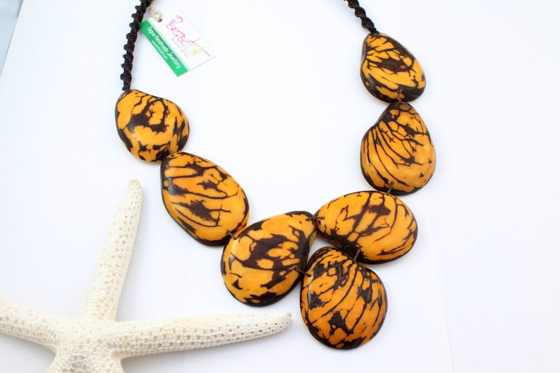May include: A necklace made of large, teardrop-shaped, yellow and brown seed pods. The necklace is strung on a black cord.