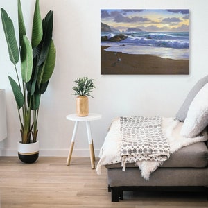 May include: A painting of a seascape with crashing waves and a sandy beach. The sky is a mix of blue and purple with a golden sunset in the distance. There are three birds walking on the beach.