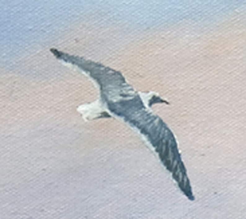 May include: An oil painting of a seagull in flight. The bird has gray and white feathers, with its wings spread wide against a backdrop of a light blue and peach sky. The artwork captures the seagull's graceful movement.