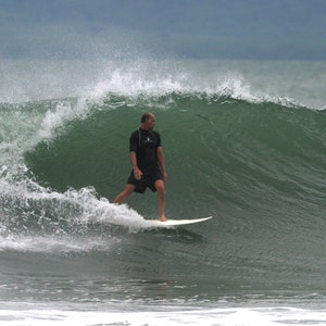 May include: A surfer rides a wave on a surfboard. The wave is green and blue, and the surfer is wearing a black wetsuit.