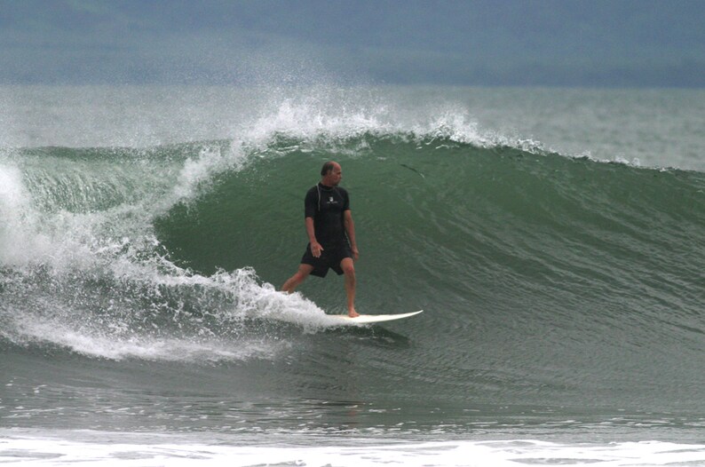 May include: A surfer rides a wave on a surfboard. The wave is green and blue, and the surfer is wearing a black wetsuit.
