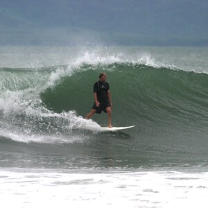 May include: A man in a black wetsuit surfs a large wave on a white surfboard.