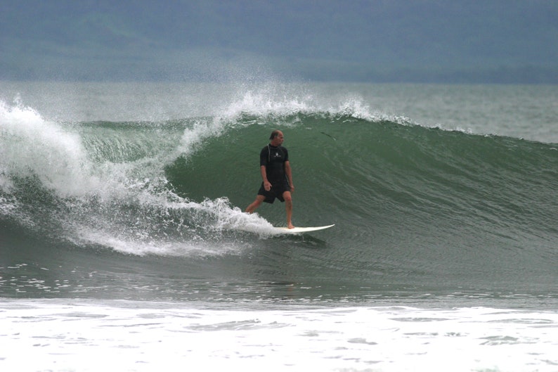 May include: A man in a black wetsuit surfs a large wave on a white surfboard.