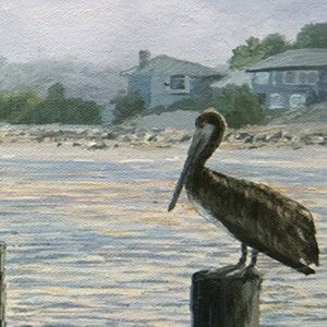 May include: An oil painting depicts a brown pelican perched on a wooden piling in the water. The background shows a shoreline with houses and trees under a hazy sky. The water has subtle reflections.