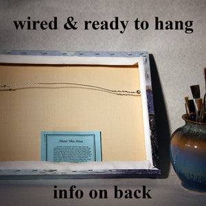 May include: The back of a canvas print with a wire hanger attached. The print has a blue and white background with a small blue card that says "About This Print" on it. The text "wired & ready to hang" is printed at the top of the image. The text "info on back" is printed at the bottom of the image.