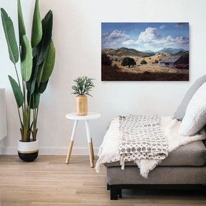 May include: A painting of a rustic wooden barn in a field with rolling hills and a large white cloud in the sky.