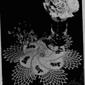 May include: A white crocheted doily with a delicate floral design. The doily is placed on a dark surface with a vase of white flowers.
