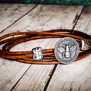 May include: A brown leather wrap bracelet with a silver bee charm and two silver beads.
