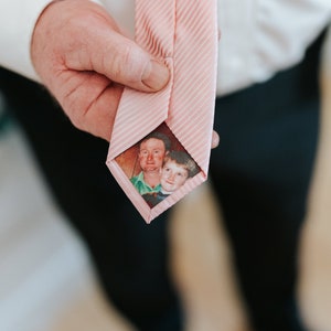 May include: A pink striped tie with a photo of two people, a man and a boy, inside the tie.
