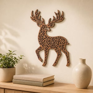 Puede incluir: Una decoración de pared de madera de color marrón oscuro con forma de ciervo de pie. El ciervo presenta intrincados patrones florales y de volutas cortados con láser en todo su cuerpo y grandes astas, creando una silueta detallada en la pared.
