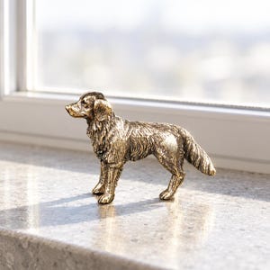 May include: A metallic bronze-toned figurine of a standing dog with detailed fur texture, pointed ears, and a long tail. The sculpture captures the canine in a side profile stance, showcasing a realistic form with a weathered, antique-style finish.