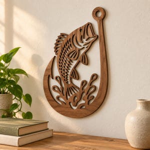 Op de afbeelding: Een donkerbruine houten wanddecoratie met een uitgesneden ontwerp van een vis aan een grote vishaak. De vis is afgebeeld terwijl deze uit gestileerde watergolven springt. Het object is gemaakt van hout met een zichtbare nerf en gladde afwerking.