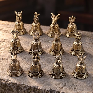 May include: A collection of twelve small, antique-style brass bells, each topped with a different animal figure representing the Chinese zodiac. The bells feature intricate embossed patterns and Chinese characters on their flared, circular bases.