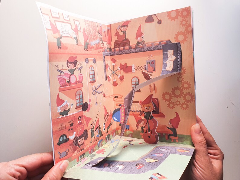 May include: A pop-up book with a colorful illustration of a workshop filled with elves making toys. The book is open to reveal a 3D pop-up of an elf playing the cello.