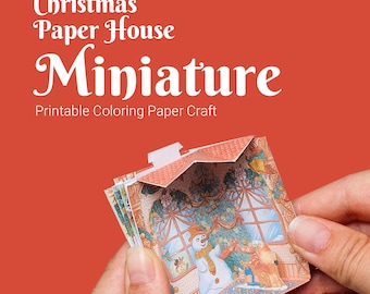 Op de afbeelding: Een miniatuur kerstpapierhuis knutselset met een sneeuwpop en een kerstboom binnenin. Het huis is gedeeltelijk opengevouwen, waardoor het interieur zichtbaar is. Het huis is bedrukt met een kleurrijk ontwerp en is klaar om in te kleuren.