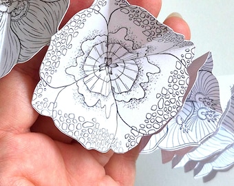 May include: A paper garland featuring a series of white flowers with black ink line art. Each flower displays intricate patterns, including stippled textures, geometric petal segments, and organic shapes, creating a detailed botanical design.