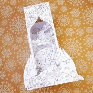 May include: A white, three-dimensional paper Christmas scene depicting a winter landscape. The scene includes a rabbit, trees, and a sleeping figure. The paper art is decorated with intricate line drawings and sits on a gold background with white snowflakes.