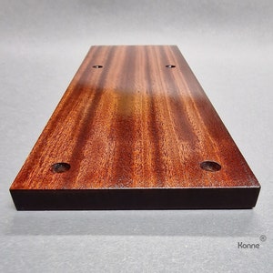 Puede incluir: Una tabla de cortar rectangular de madera con un tinte marr&oacute;n oscuro. La tabla tiene cuatro agujeros perforados, dos a cada lado. La tabla est&aacute; hecha de una madera con un patr&oacute;n de veta pronunciado.