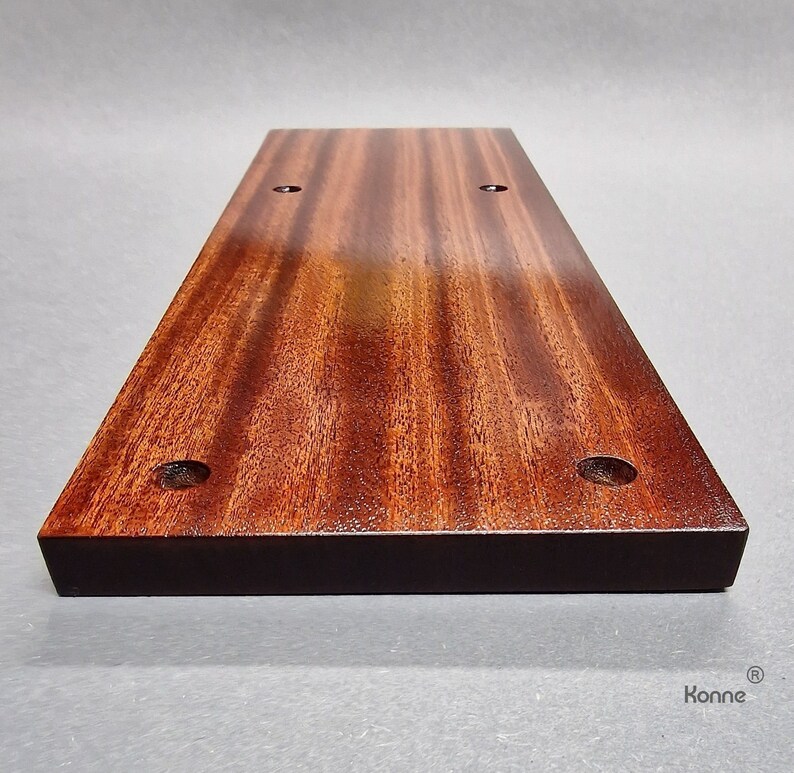 Puede incluir: Una tabla de cortar rectangular de madera con un tinte marr&oacute;n oscuro. La tabla tiene cuatro agujeros perforados, dos a cada lado. La tabla est&aacute; hecha de una madera con un patr&oacute;n de veta pronunciado.