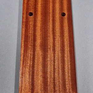 Puede incluir: Una placa rectangular de madera de color marr&oacute;n rojizo intenso con un patr&oacute;n de veta de madera. La placa tiene cuatro agujeros perforados a intervalos regulares.