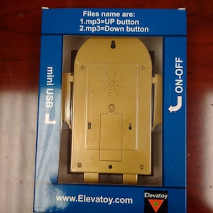May include: A gold-coloured elevator sound effect device with a mini USB port, an on/off switch, and the text "Files name are: 1.mp3=UP button 2.mp3=Down button" and "www.Elevatoy.com" printed on the packaging.