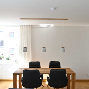 May include: A dining room with a wooden table and four black chairs. Three white pendant lights with wooden accents hang from a wooden rail.
