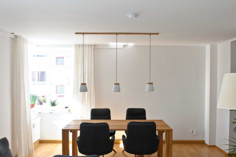 May include: A dining room with a wooden table and four black chairs. Three white pendant lights with wooden accents hang from a wooden rail.
