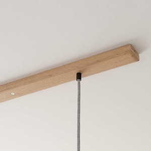May include: A close-up of a wooden ceiling mount with a gray cord hanging from it. The cord is attached to a black ceiling plate.