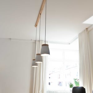 May include: Three white pendant lights with wooden tops hang from a wooden rail on a white ceiling. The lights are over a wooden table with black chairs.