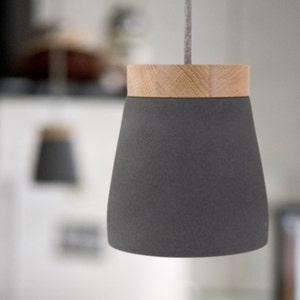 Könnte beinhalten: Eine graue Keramik-Pendelleuchte mit einem Holzdeckel. Die Leuchte hängt an einem Kabel.