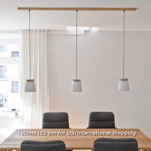 May include: Three white pendant lights with wooden tops hang from a wooden rail above a wooden table with four grey chairs. The text "100cm/120 cm for US/International Shipping" is printed on the table.
