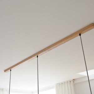 May include: A wooden ceiling track with three black cords hanging down from it. The cords are attached to the track with black metal fixtures.